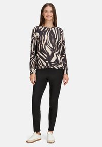 Langarmshirt met een zwart en beige abstract patroon, gecombineerd met zwarte slim-fit broek en witte sneakers.