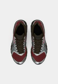 Piros és ezüst hálós sportcipők barna részletekkel. Kerek orrúak, fűzősek, és a felsőrészen texturált mintázat található a légáteresztés érdekében.