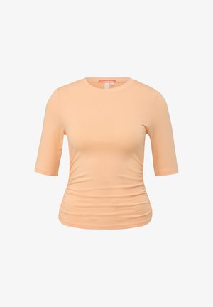 Brzoskwiniowy t-shirt z krótkim rękawem, okrągłym dekoltem, z efektem marszczenia po bokach oraz miękką, gładką fakturą. Brak widocznych logo i wzorów.