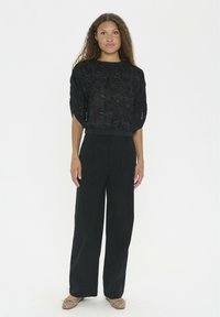 Black cropped top with textured pattern, paired with high-waisted, wide-leg black trousers. Person wears beige studded slip-on shoes.