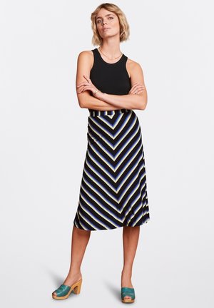 Top a righe nera abbinato a una gonna a lunghezza ginocchio con un motivo a zig-zag nei colori navy, crema e blu chiaro. Mostrate delle mules con tacco in legno.