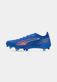 Blauer Sport-Schuh mit Metallschrauben und roten und weißen Logo-Details, entworfen für den Einsatz im Freien auf Gras oder Kunstrasen.
