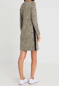 Robe à imprimé léopard avec des manches longues, un col rond et des accents noirs sur les côtés. Tissu doux, longueur genou, portée avec des baskets blanches.