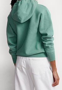 Felpa con cappuccio verde menta dal taglio rilassato, con polsini e orlo a coste, abbinata a jeans bianchi con tasche posteriori. Materiale in cotone accogliente.