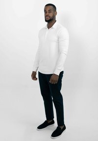 Witte lange mouwen polo, zwarte slim-fit broek en zwarte instapschoenen met witte zolen. Eenvoudig ontwerp, effen kleuren en een aangesloten stijl.