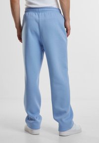 Lyseblå svedbukser med en glat overflade, elastisk talje, og tapered ben, parret med hvide sneakers.