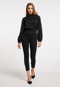 Top lung cu mâneci lungi din satin negru, cu guler înalt și talie elastică, combinat cu pantaloni negri ajustați și tocuri ascuțite negre.