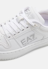Hvite lær sneakers med snøring, som har en teksturert overflate, logo-detalj og et mønstret gummisåle.