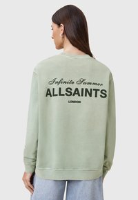 Felpa oversized verde chiaro con una texture morbida. Presenta la scritta "Infinite Summer" e "ALLSAINTS LONDON" in evidenza sul retro.