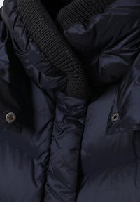 Mornarska puf jakna s crnim pletenim ovratnikom, metalnim kopčama i quiltanom teksturom za izolaciju i toplinu.