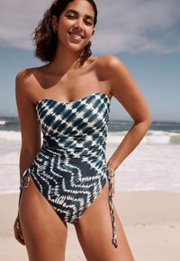 Ühes tükis ujumistrikoo sinakasrohelises ja valges toonis, ilma õlapaelteta, voltidega tekstuuri ja reguleeritavate kinnitustega puusadel. Sile kangas.