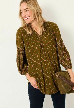 Olive green floral blouse with puffed sleeves, featuring a V-neckline and embroidered accents. Paired with a textured green handbag.