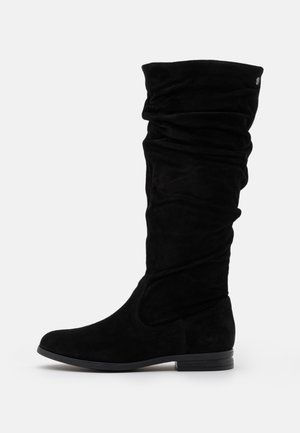Czarny zamszowy kozaki za kolano z luźnym cholewką, niskim piętą na słupku, zaokrąglonym noskiem i bocznym przeszyciem na białym tle.