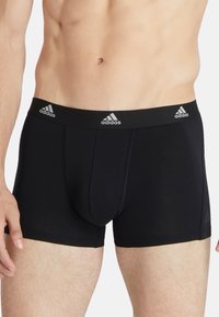 Calzoncillos bóxer negros hechos de tela suave con un ajuste ceñido. Presentan una cinturilla ancha negra con tres logotipos blancos de Adidas.