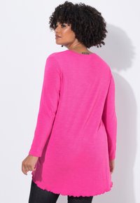 Maglietta a maniche lunghe di un vivace colore rosa con orlo a scallop, realizzata in un tessuto morbido e testurizzato. Presenta un colletto rotondo e una vestibilità rilassata.