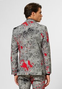 Gray textured suit jacket with a bold abstract pattern featuring gray, black, and red splashes. Standard lapels and back vent detail.