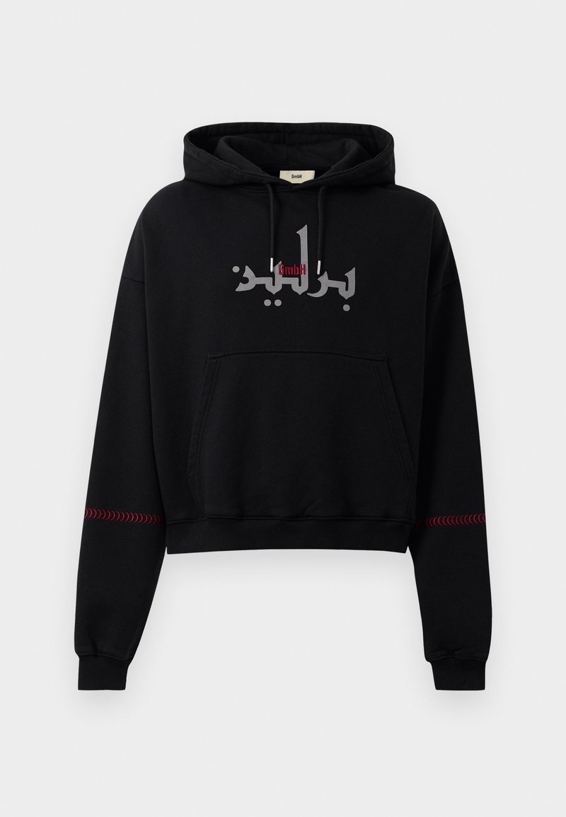 Sort cropped hoodie med snor, prydet med arabisk tekst i sølv og røde detaljer på ærmerne. Blødt stof, design med kengurulomme.