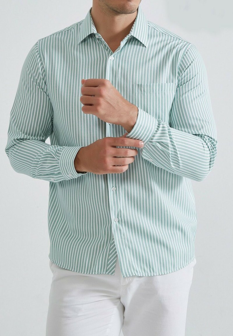 Chemise à rayures vert clair et blanche, boutonnée, avec col et une poche poitrine, possédant des manches longues et une coupe ajustée.
