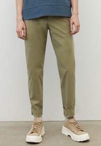 Beżowe chinosy o slim fit i podwiniętych mankietach, w połączeniu z jasnobeżowymi trampkami. Materiał wydaje się gładki i lekki; minimalistyczny design.