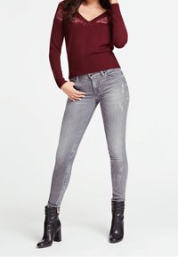 Burgundy neule, jossa on pitsikoristeita, yhdistettynä vaaleanharmaisiin slim fit -farkkuihin, joissa on kulutettuja yksityiskohtia, sekä mustiin nilkkureihin, joissa on paksu korko.