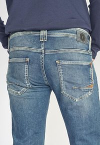 Vervaagde blauwe denim jeans met een rechte pasvorm, voorzien van achterzakken met subtiele stiksels en een zwart leren label bij de tailleband.
