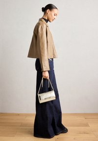 Light brown leather cropped jacket over a black turtleneck, paired with dark blue wide-leg jeans and a silver chain handbag.
