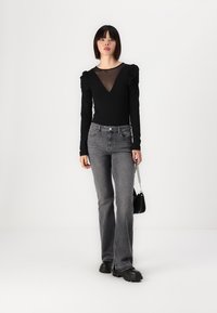 Black long-sleeve bodysuit with a sheer neckline, paired with faded grey flared jeans and chunky black boots. Simple chain handbag accent.