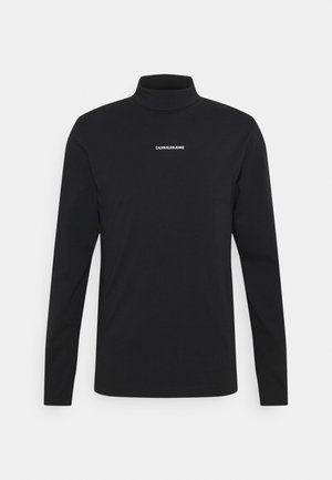 Schwarzes, langärmliges Rollkragenhemd mit dem Text "CALVIN KLEIN JEANS" mittig auf der Brust vor einfachem Hintergrund.