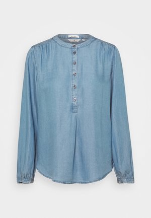Blusa di jeans azzurro chiaro a maniche lunghe con scollo rotondo e cinque bottoni sulla patta anteriore, con lievi arricciature su spalle e polsini.