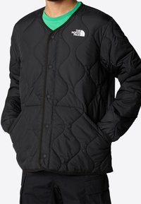 Czarna pikowana kurtka z dekoltem w serek, zapięciem na napy, bocznymi kieszeniami i logo The North Face na lewej piersi.