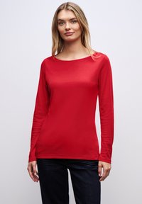 Rode lange mouwen top van soepel stof met een ronde halslijn en een aansluitende snit, gecombineerd met donkere jeans. Geen opvallende patronen of accenten.