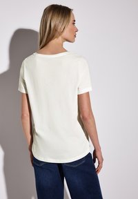 T-shirt crème à manches courtes avec un décolleté arrondi, en coton doux et coupe décontractée, associé à un jean bleu foncé.