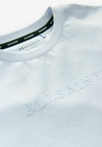 Šviesiai mėlynos medvilninės marškinėlių su apvaliu kaklu, ant priekinės dalies iškeltu "ALLSAINTS" logotipu ir tamsiu etiketė vidinėje apykaklės pusėje.