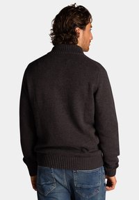 Donkergrijze gebreide trui met een hoge kraag en ribgebreide manchetten en zoom, gecombineerd met blauwe denim jeans. Soepele textuur en klassieke pasvorm.