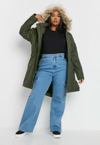 Olivgrön parkas med foder i päls, dragkedjestängning, dragsko i midjan; ihopparad med högmidjade blå jeans med cargofickor.