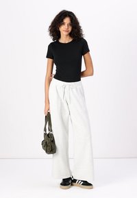 Sort kortærmet skjorte parret med lysegrå, vide sweatpants. Modellen bærer en grøn taske og har sorte sneakers med hvide striber på.