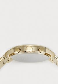 Vue de côté d'une montre-bracelet dorée montrant la couronne et deux boutons-poussoirs sur un bracelet en métal lié.