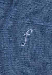Plavi pleteni materijal s blagim izvezom malog slova "f" u nešto svjetlijoj nijansi plave. Tekstura je glatka i zanimljiva.