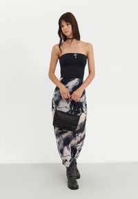 Svart strapless topp kombinerad med en lång, tie-dye kjol i nyanser av marinblått och kräm. En svart vadderad handväska och svarta ankelboots.
