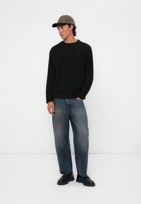 Svart langermet skjorte, lyseblå rette jeans og svarte sko. En rutete caps fullfører antrekket og tilføyer tekstur og mønster.