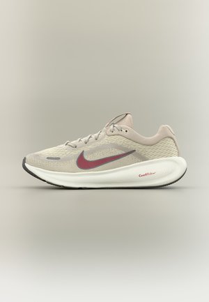 Jasnobeżowy but biegowy Nike z czerwonym logo Swoosh i białą amortyzowaną podeszwą oznaczoną ComfiRide, pokazany z boku na neutralnym tle.