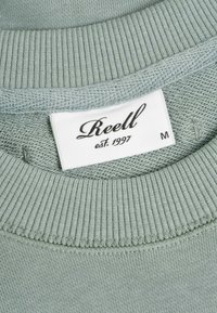 Light green knit sweater with ribbed collar and white label reading "Reell est. 1997" and size "M" inside the neckline.