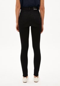 Vaqueros negros de cintura alta con una forma ajustada, textura suave, dos bolsillos traseros y una etiqueta de marca en la cintura.