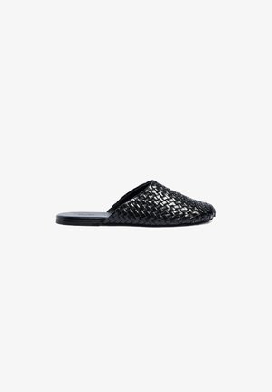 Zwarte gevlochten leren slip-on mule met platte zool en gesloten puntige neus, zijaanzicht op een witte achtergrond.