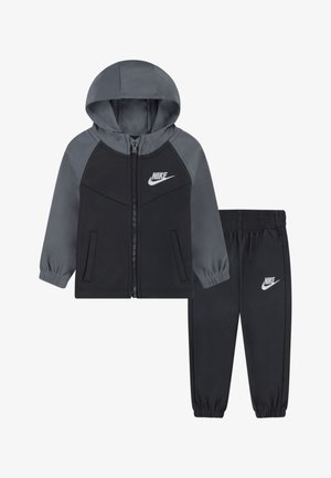 Zwart en grijs Nike trainingspak met een rits-hoodie en elastische broek. Kenmerkt zich door zachte stof, elastische boorden en het kenmerkende logo op beide stukken.