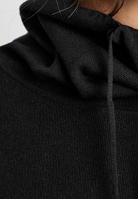 Hoodie noir en tissu texturé, avec un cordon de serrage au niveau du col et un matériau froncé pour un ajustement près du corps.