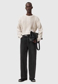 Bohatý krémový sveter s pleteným vzorom, tmavé šedé denimové nohavice, čierna kožená taška cez rameno a čierne topánky s bielymi akcentmi.