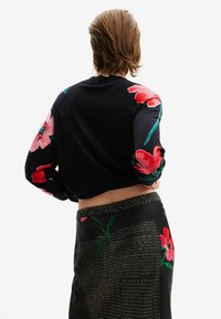 Maglione nero corto con motivi floreali colorati sulle maniche; abbinato a una gonna nera con testo e motivi floreali.