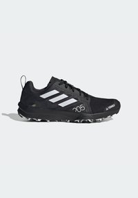 Scarpa da corsa nera con parte superiore in mesh testurizzato, design a tre stripe bianche e suola in gomma nera con tacchetti per la trazione. Presenta una linguetta per facilitare la calzata.