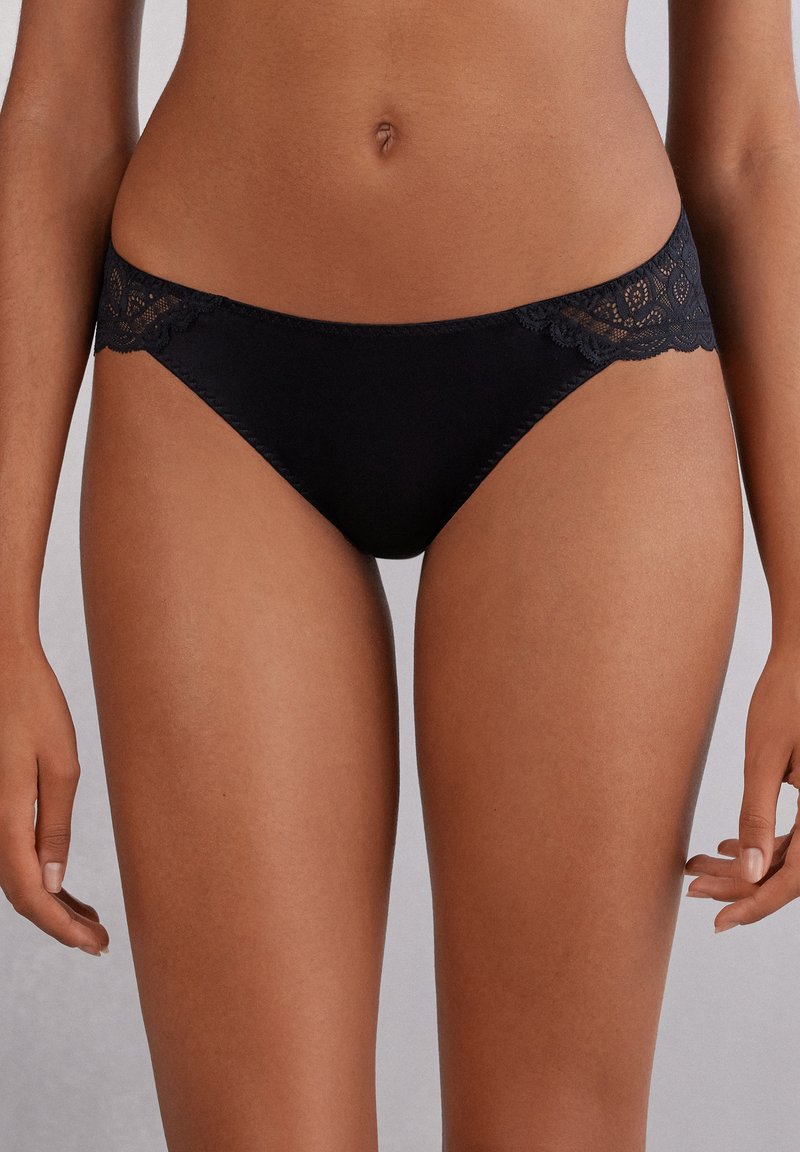 Zwarte bikini met kantafwerking, met een gladde stoffen body en een decoratieve kanten tailleband. Ontworpen voor comfort en subtiele elegantie.